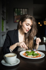 Smiling young woman eating fresh salad in restaurant