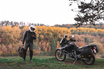 Fototapeta premium Rider standing with backpack. adventure motorcycle, Motorcyclist gear, A motorbike driver looks, concept of active lifestyle, enduro travel road trip. Evening, autumn. Tourist traveler. copy space