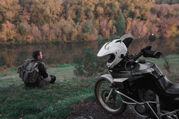 Obraz premium Lonley concept, man is sitting alone and look at the distance. Adventure motorcycle, Motorcyclist, A motorbike driver looks, concept of active lifestyle, enduro travel road trip, destination