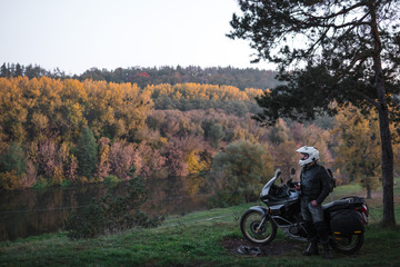 Rider standing with adventure motorcycle, Motorcyclist gear, A motorbike driver looks, concept of active lifestyle, enduro travel road trip. Evening, autumn. Tourist traveler. copy space