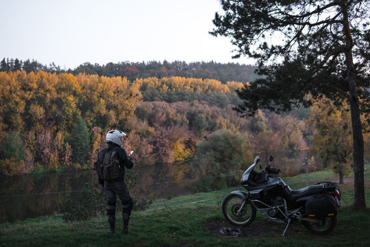 Rider standing with adventure motorcycle, Motorcyclist gear, A motorbike driver looks, active lifestyle, enduro travel road trip. Evening, autumn. Tourist traveler. copy space, use gadget, enternet