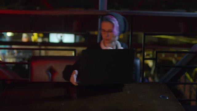Zoom in of young female programmer sitting down at caf&eacute; table, putting laptop on table and starting typing on keyboard