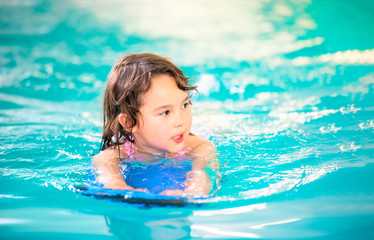 Smiling girl has fun with floating board in swimming pool