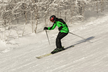 Fototapeta na wymiar ASHA, RUSSIA - 27 april 2011: male skier moves down the slope against trees in the snow, wearing black and green ski suit mask and helmet in the hands of sticks, editorial photo 
