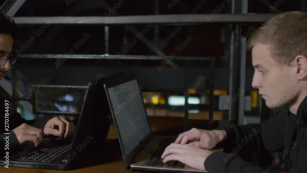 Aufkleber panning of two young multiethnic men in hoodie sitting at café table in front of each other and typi