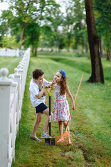 Cheerful little girl with rake and boy digging with shovel near the wooden fence in the park....