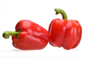 Composition of two Bulgarian red peppers with green branches on a neutral white background.