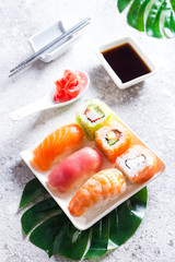 Set of sushi and maki roll and green leaves palm on stone table. Top view