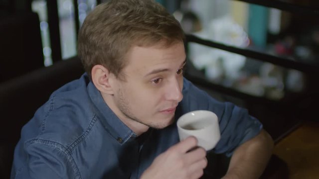 High angle view of Caucasian man drinking tea from tea cup and talking to interlocutor sitting in front of him