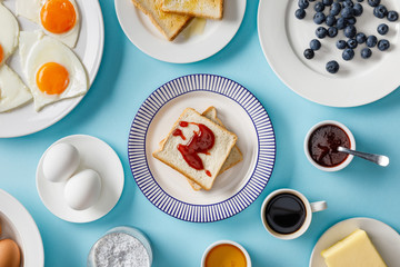 top view of table setting for breakfast and toasts with jam on plates on blue background
