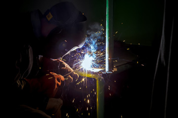 A welder at work.  Sparks flying. Welder in mask at work. Profession of a welder. Sparks around. Welding metal. Dark background. Bright light.