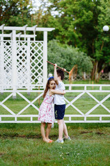 Cheerful little girl and boy with rake in summer garden. Brother and sister playing in the summer park. Best friends. Childhood concept.