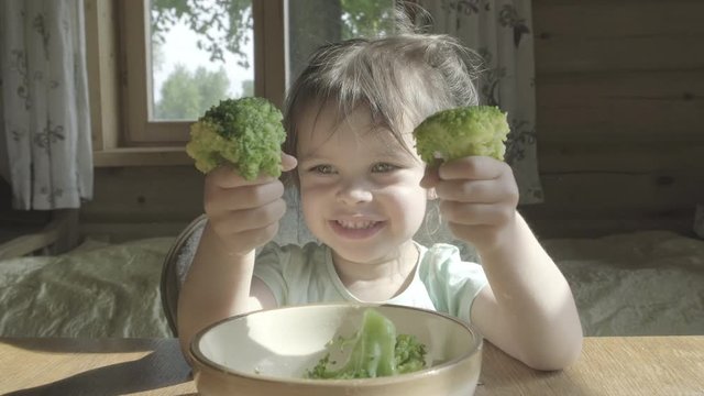 Happy little girl hate eating broccoli vegetables on a plate with hands