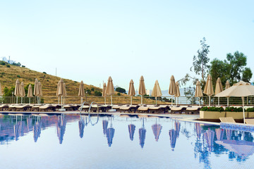 Fototapeta na wymiar Outdoor luxury swimming pool, umbrellas, sun beds with reflection in the water at the holiday, background is beautiful mountain, relax place.