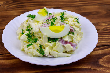 Salad with chinese cabbage, onion, sausage, eggs and mayonnaise on wooden table