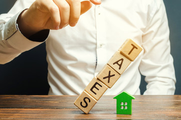 Wooden blocks with the word Taxes fall on a miniature house. The concept of the tax burden on housing, apartment, property. Mortgage. Taxation. Taxpayer. Commercial real estate. Soft selective focus