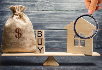 A money bag and wooden blocks with the word Buy and a miniature house on scales. The accumulation of money for the purchase of real estate. Buying a home. Buy a property. Reaching the goal.