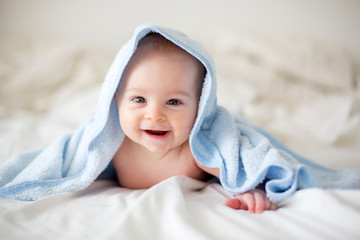 Cute little baby boy, relaxing in bed after bath, smiling happily
