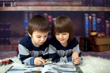 Two little children, boys, reading a book with magnifying glass