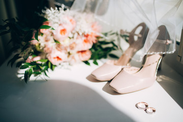 Brides wedding shoes with a bouquet with roses and other flowers on tha arm chair