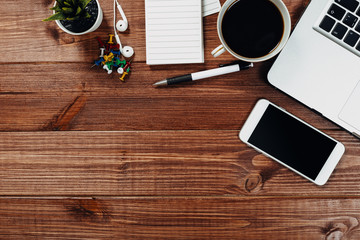 Wood office desk table with laptop, cup of coffee and supplies.