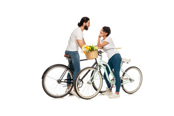 bearded latin man looking at attractive woman sitting on bicycle isolated on white