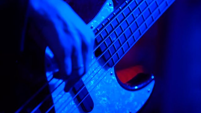 Male musician playing bass guitar, shooting in a nightclub with artificial light, close-up and slow motion