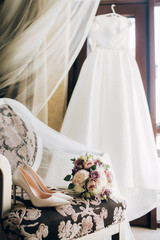 Brides wedding shoes with a bouquet with roses and other flowers on tha arm chair