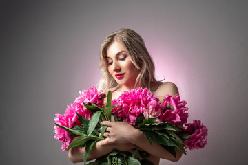 Fashion photo of a beautiful young woman with a bouquet of pink flowers, with make-up and hairstyle