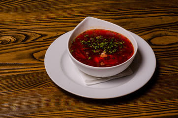 Beats soup, borsch with sour cream; bead and pickles on a background. borsch in a white dish, slices of bread on a wooden cutting board, whole pickles in a wooden dish.