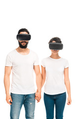 latin man and woman wearing virtual reality headsets and holding hands while standing isolated on white