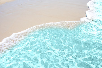 Soft wave of turquoise sea water on the sandy beach.