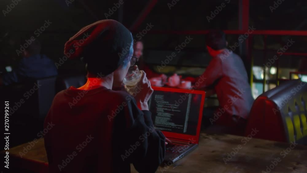 Poster back view of caucasian female software developer sitting at laptop in café, typing program code, dri