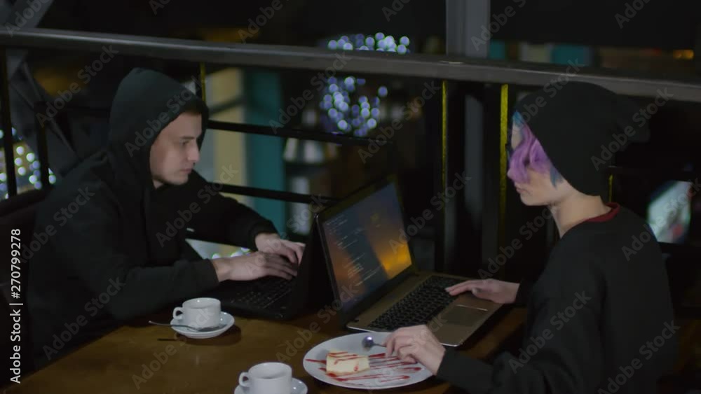 Aufkleber lockdown of two hackers sitting at café table in front of each other and programming. woman eating d