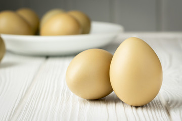 Two pheasant eggs in the foreground and a plate with eggs in the background on a wooden white table