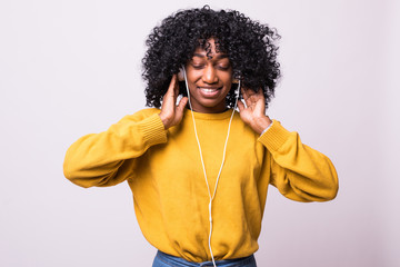 Adorable african woman in yellow sweater singing and having fun while listening to music using wireless earphones isolated over white background