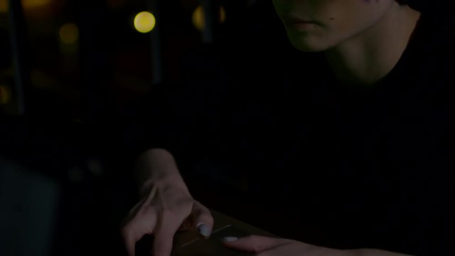 Tilt up of female hipster sitting at laptop in darkness and typing message