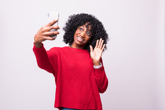 Portrait of a smiling young african woman taking selfie with mobile phone or video call over white background
