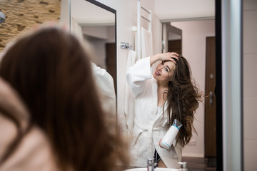 Portrait of a gorgeous young woman drying her hair with a blow dryer in the bathroom
