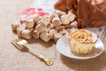 Board game lotto and homemade biscuit on saucer. Wooden lotto barrels in bag.