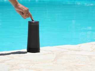 Cropped image of a man using a portable speaker with voice assistant and touch technology near the outdoor swimming pool.