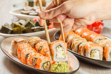 Male hand with two chopsticks holding Uramaki Philadelphia sushi roll.