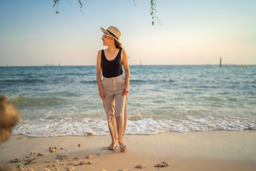 relaxing time concept with traveler girl wearing sunglasses and hat walking in the sea beach in beautiful sunset time
