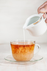 Milk poured into cup of tea by man hand