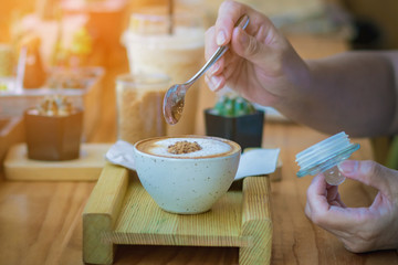 Woman pouring sugar into a white cup of coffee