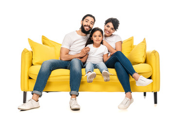 happy latin parents smiling while sitting on sofa with adorable daughter isolated on white