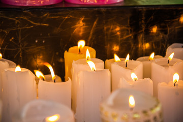 Several white candles lit for prayers with only the centered candles in focus.