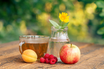 Ripe fruits, calendula flower with a stem in a glass flask and cup of green tea.