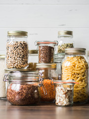Various cereals and seeds - pumpkin seeds, beans, rice, pasta, flax, lentils, almond slices, bulgur in glass jars on the table in the kitchen