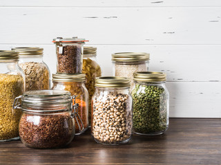 Various cereals and seeds - peas split, beans, rice, pasta, oatmeal, flax, lentils, bulgur in glass jars on the table in the kitchen